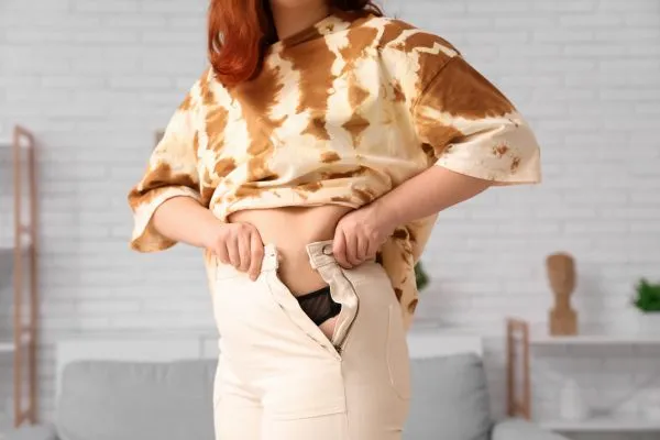 Image of woman trying to do her trousers up after pregnancy weight gain Croydon